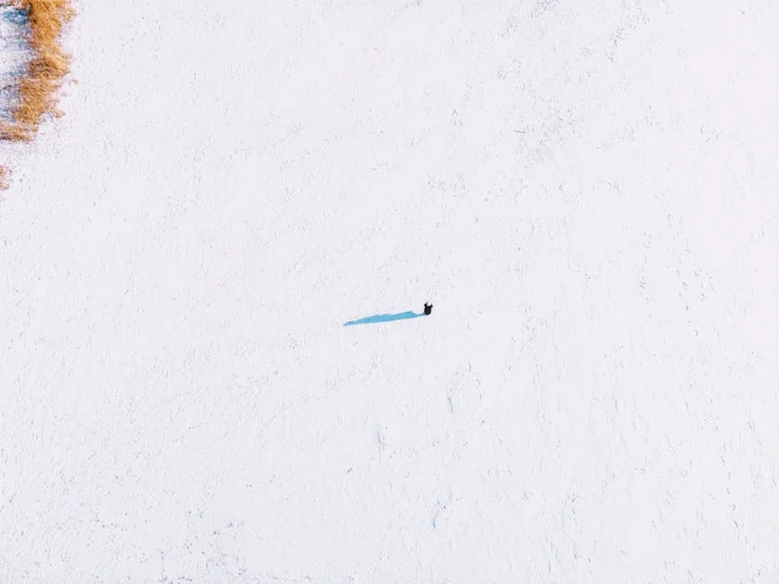 Aerial shot of a solitary figure on a vast snowy field in Harbin, China, capturing winter's stark beauty.